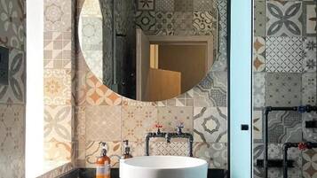 Un baño con espejo redondo, lavamanos blanco y baldosas estampadas.