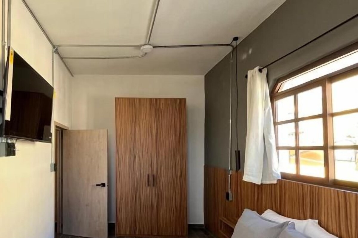 Un dormitorio con cama, armario, ventana con cortinas y puerta.
