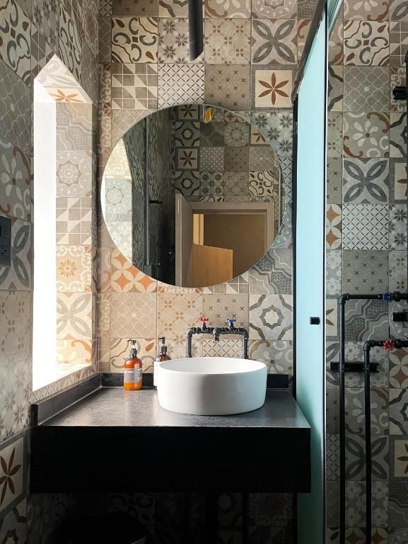 Un baño con un espejo redondo, un lavabo blanco y baldosas estampadas.