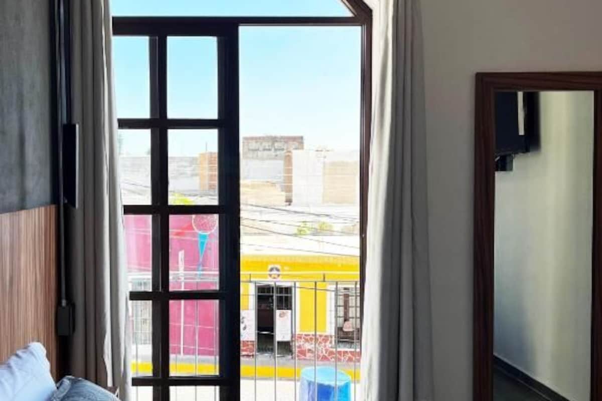 Quarto com cama, janela com cortinas e vista para o exterior.
