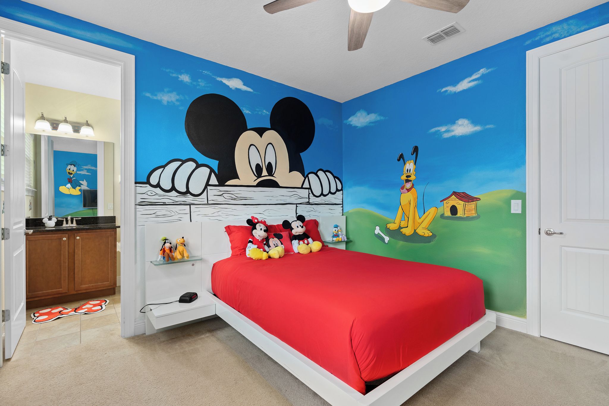 A bedroom with a red bedspread, Mickey Mouse mural, and a green landscape wall.