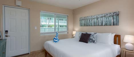 Ein Schlafzimmer mit einem Bett, einem Deckenventilator, einem Fenster mit Jalousien, einer Tür und einem an der Wand hängenden Kunstwerk.
