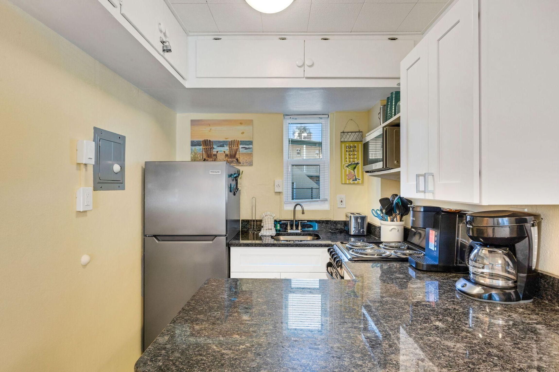 A compact kitchen with a stainless steel refrigerator, a gas stove, and a coffee maker.