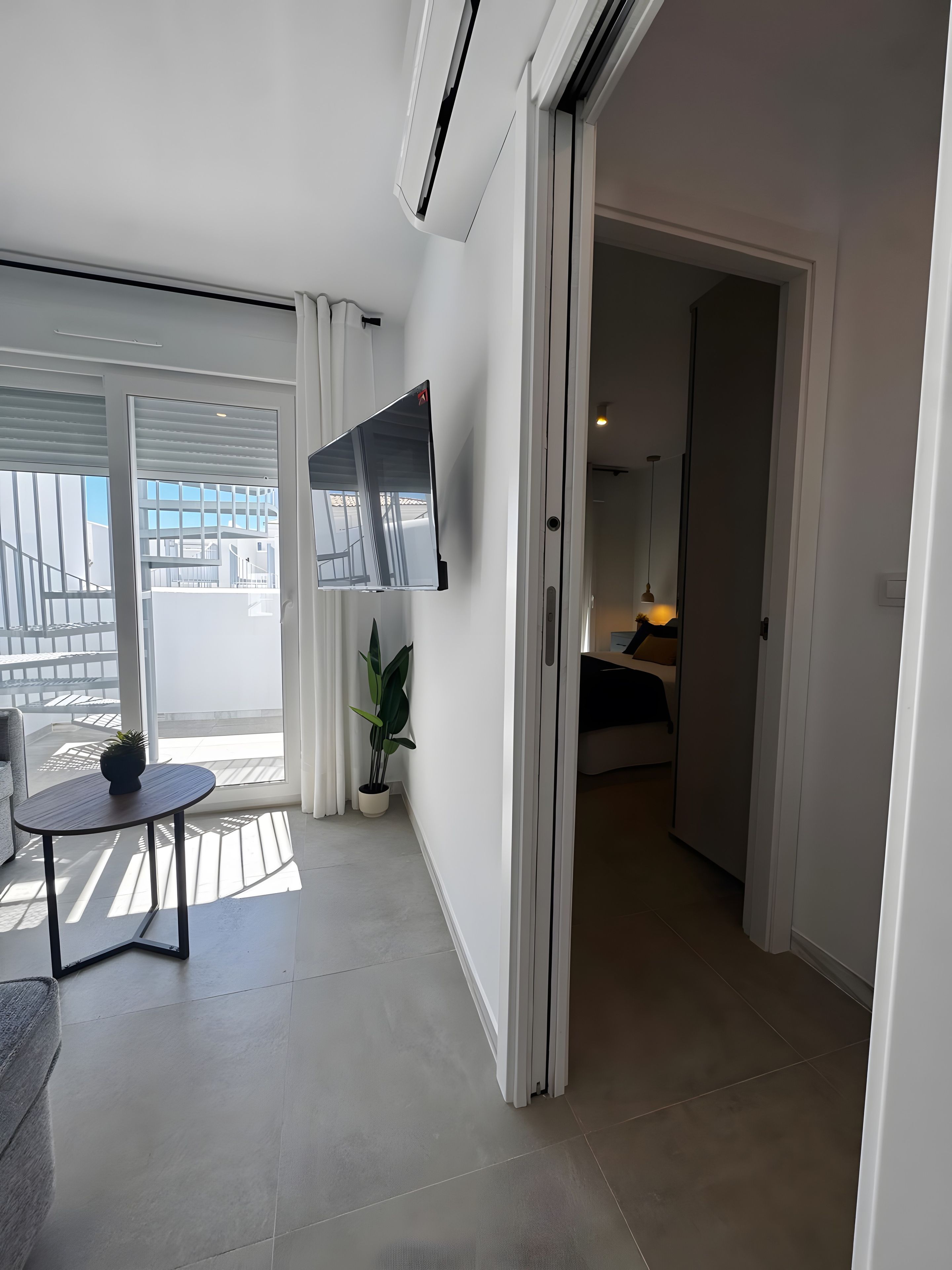 Un intérieur moderne avec un balcon, un téléviseur à écran plat fixé au mur, une plante en pot et un coin repas.