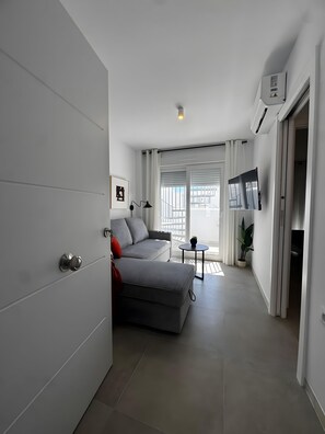 Una sala de estar moderna con un sofá gris, una mesita redonda y un televisor de pantalla plana montado en la pared.