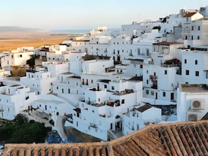 A densely packed white building with multiple levels and balconies, surrounded by a hilly landscape. - Apartment 'La Barrosa Room' with Private Terrace, Garage Space and Air Conditioning (Vejer de la Frontera)