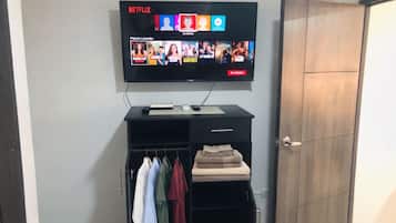 A flat-screen TV mounted on a wall displaying various Netflix shows. Below the TV, there is a black entertainment unit with a remote control.