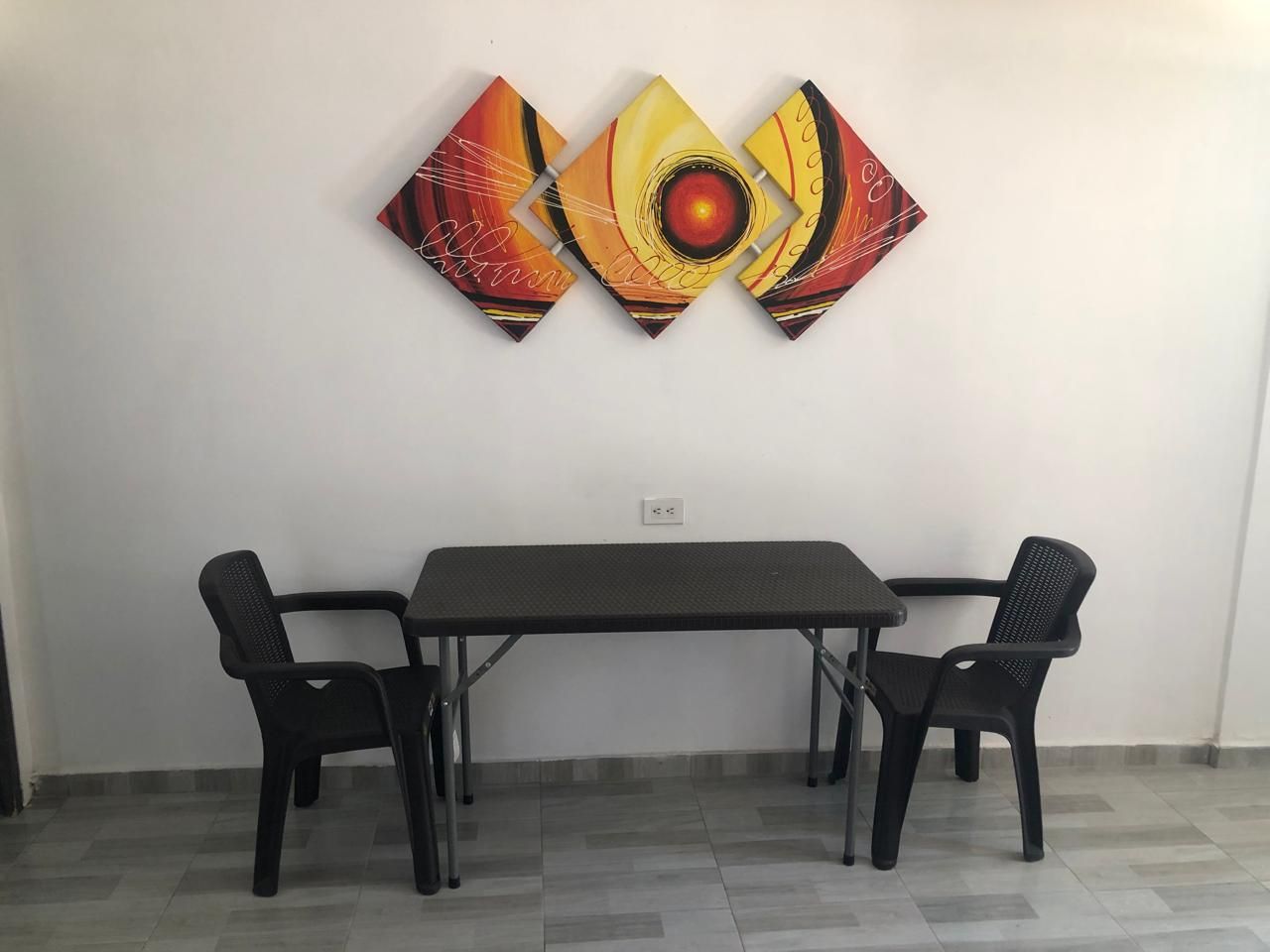 Un área de comedor con una mesa y sillas, una obra de arte colgada en la pared y piso de baldosas.