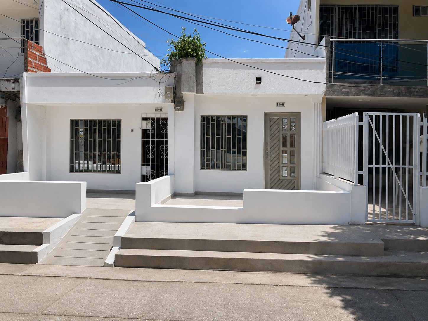 A white building with a gated entrance, a small porch, and a staircase leading to the entrance.