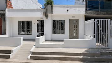 A white building with a gated entrance, a small porch, and a staircase leading to the entrance.