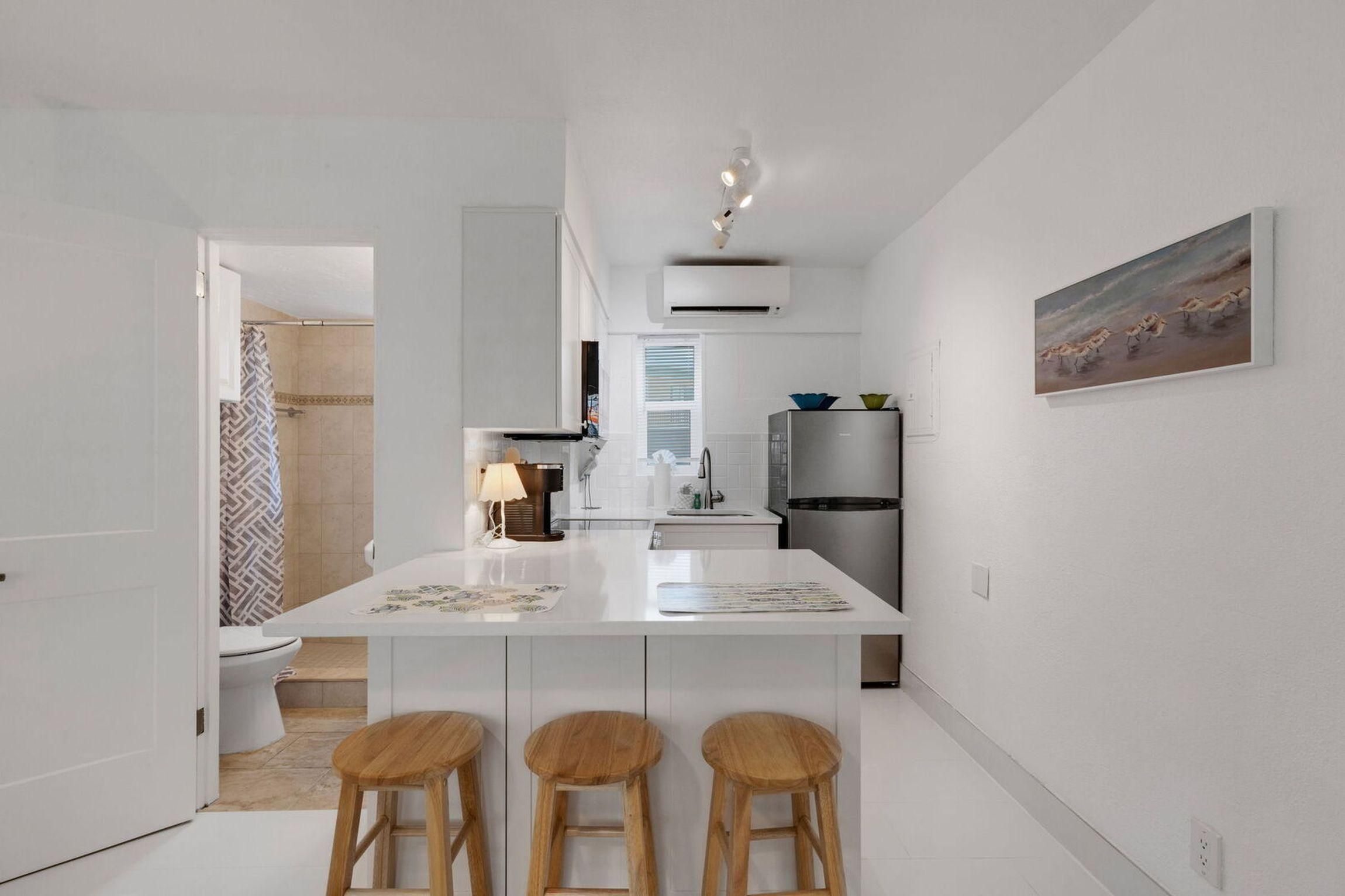 Une cuisine moderne avec un îlot central, des tabourets de bar et un tableau au mur.