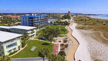 A coastal hotel with multiple buildings, a beach, and a clear sky.