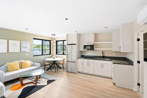 Une cuisine moderne avec des meubles blancs, un réfrigérateur en acier inoxydable et un plan de travail noir.