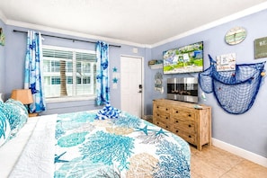 Quarto com uma cama, cômoda de madeira, televisão e janela com cortinas.