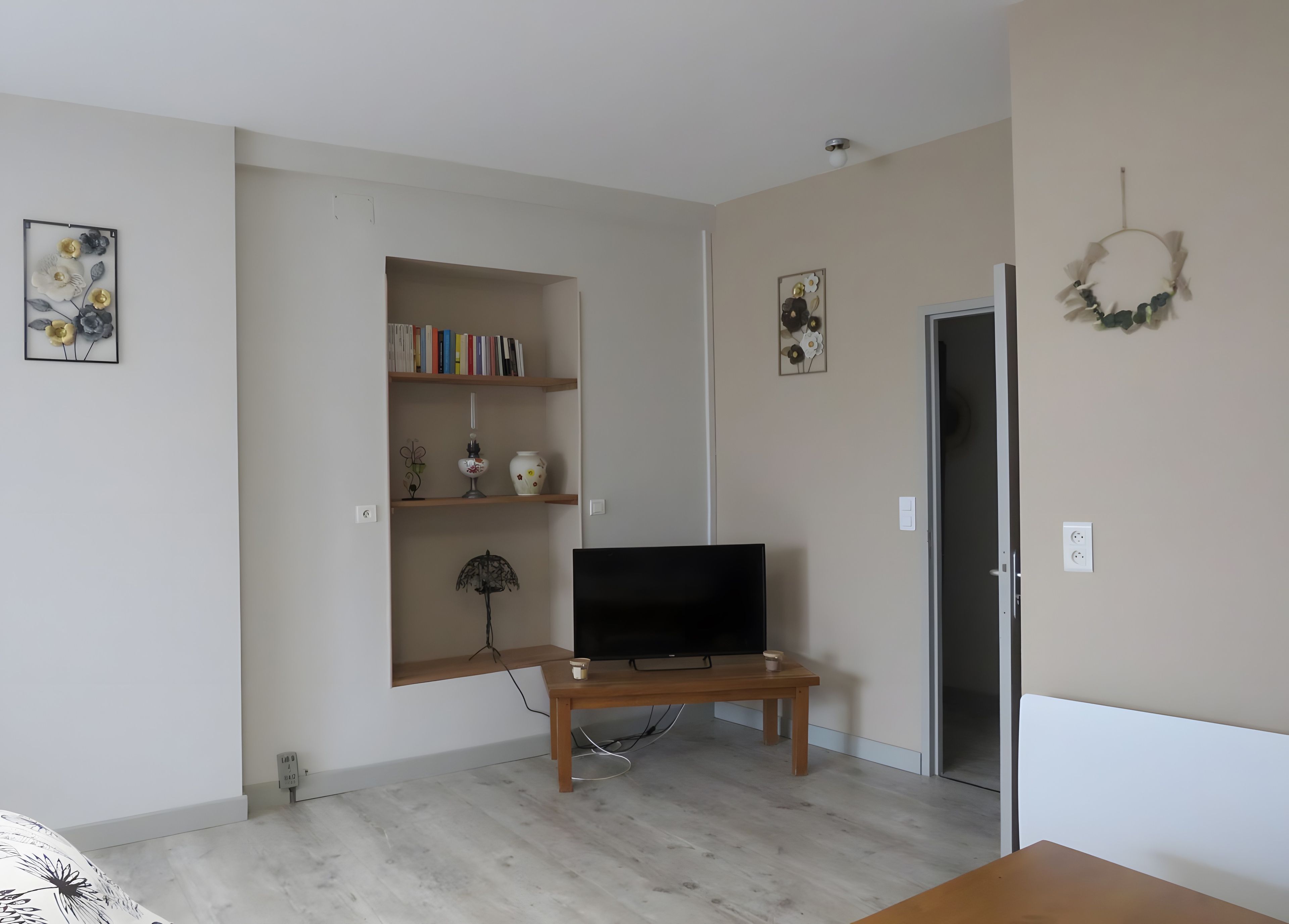 Un salon avec un téléviseur à écran plat posé sur un meuble en bois, une bibliothèque remplie de livres et d’objets décoratifs, et une porte ornée d’une guirlande.
