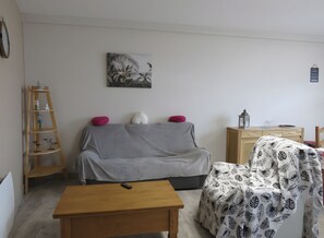 En stue med en grå sofa, et træbord, en lille træstige og et billede på væggen.
