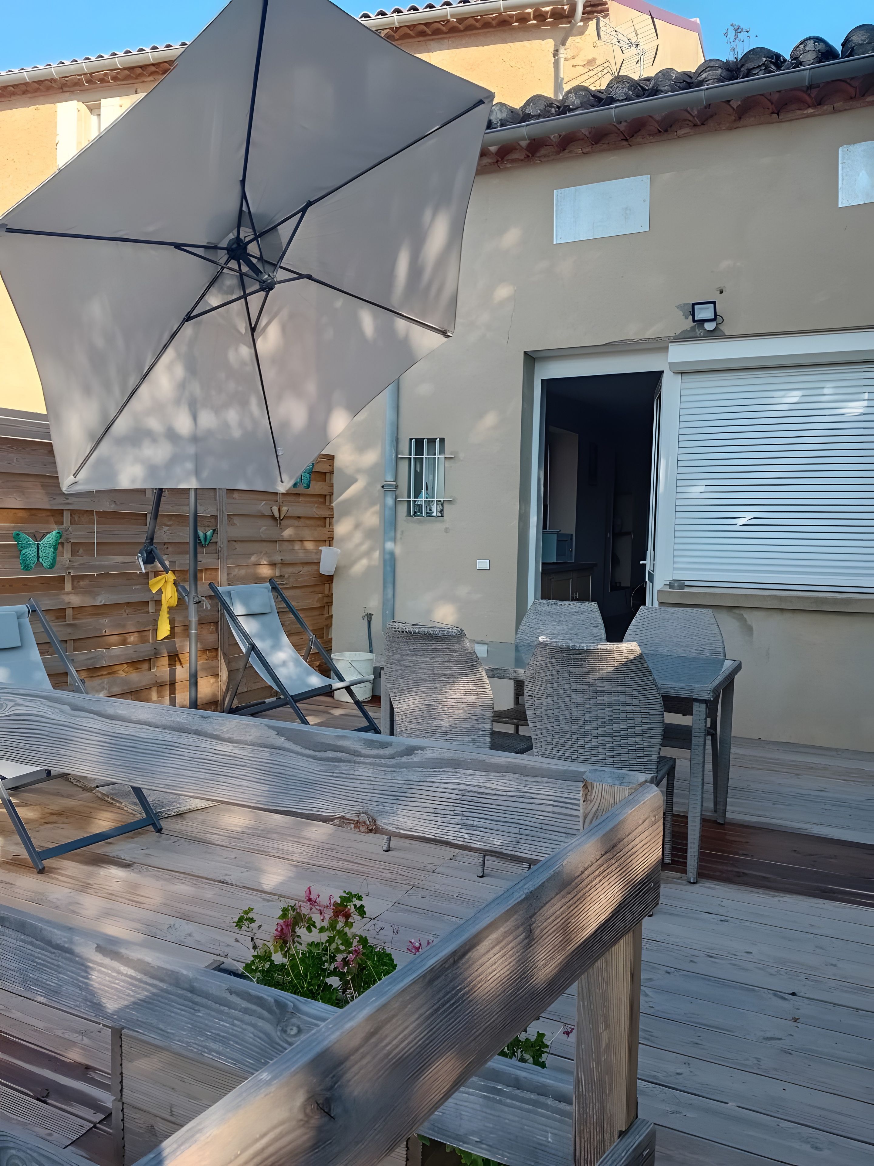 Eine Terrasse im Freien mit Holzdeck, großem Sonnenschirm und Gartenmöbeln.