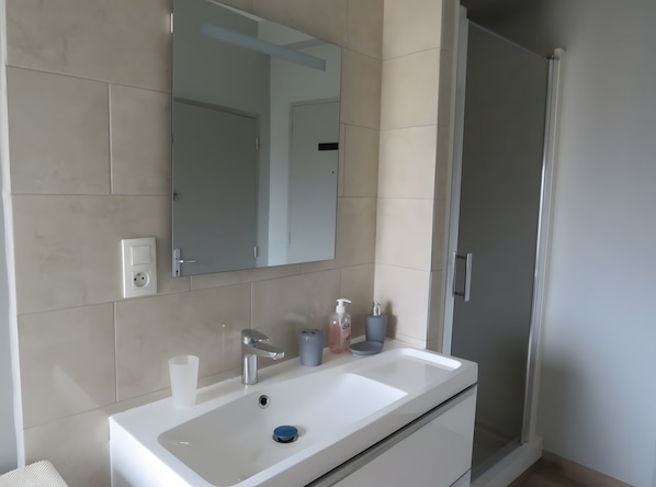 Ein Badezimmer mit weißem Waschbecken, Spiegel, Dusche und Toilette.