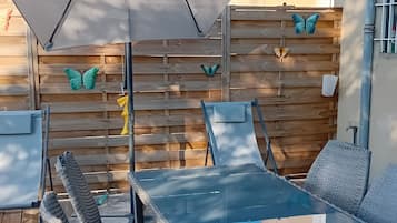 En uteplats med ett glasbord och stolar, ett stort parasoll och dekorativ väggkonst med fjärilsmotiv.