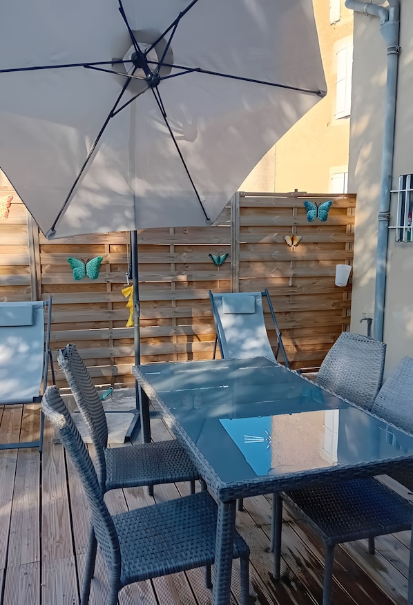 En udendørs patio med et glasbord og stole, en stor parasol og dekorativ vægkunst med sommerfugle.