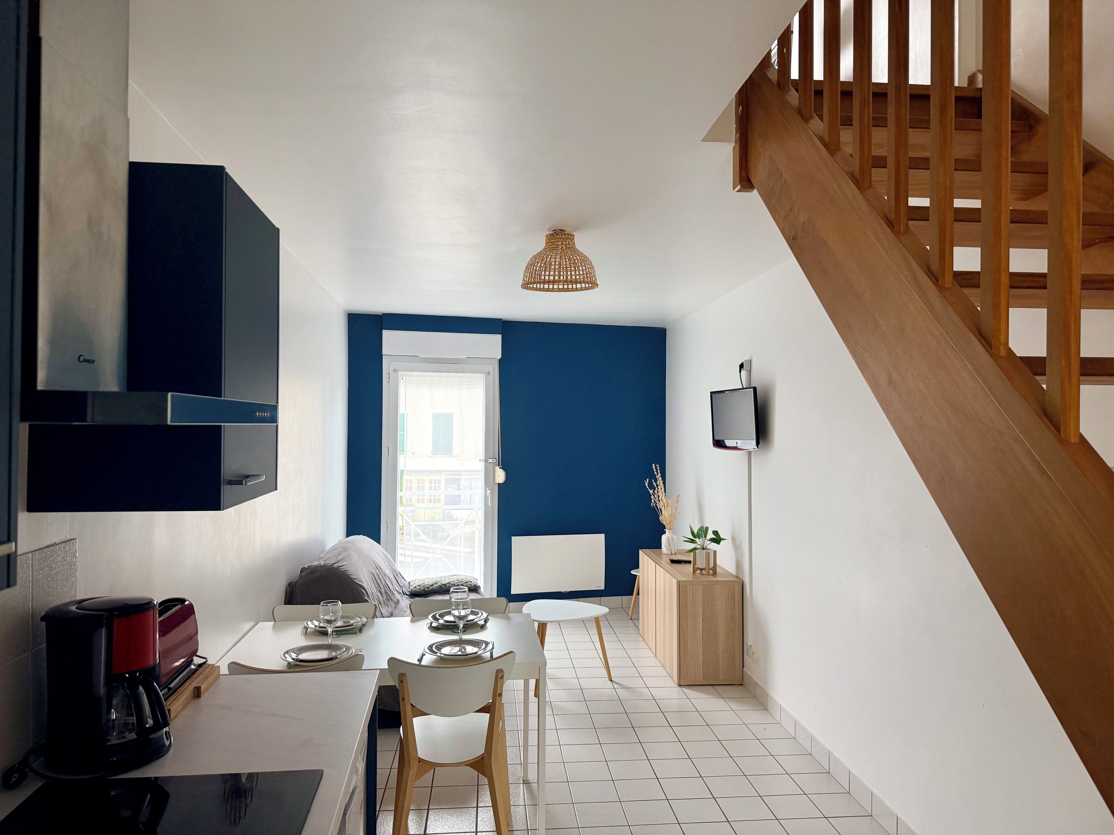 A modern kitchen with a dining area, a staircase, and a view through a door.
