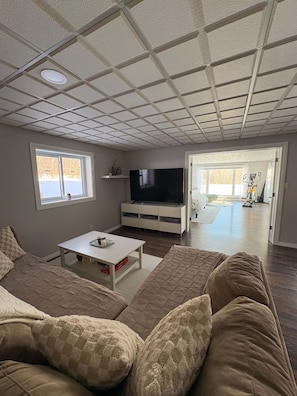 A living room with a television, sofa, coffee table, and a view of the backyard. - Large Luxurious Apartment with Mountain View (5 minutes from airport & ski hill) (Thunder Bay)