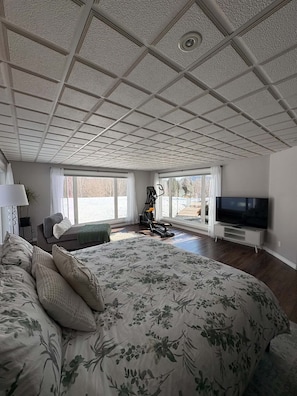 A spacious bedroom with a large bed, a TV, and a view of the outdoors. - Large Luxurious Apartment with Mountain View (5 minutes from airport & ski hill) (Thunder Bay)