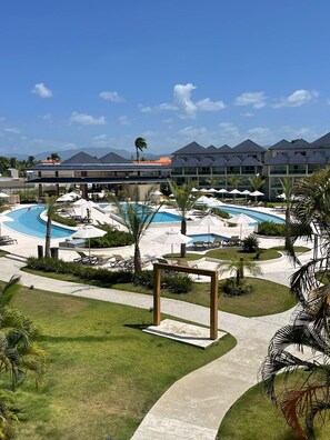 A resort with a large swimming pool, sun loungers, and palm trees. - 1BR Penthouse - Private Beach, Pool & Ocean Views (Playa Dorada)