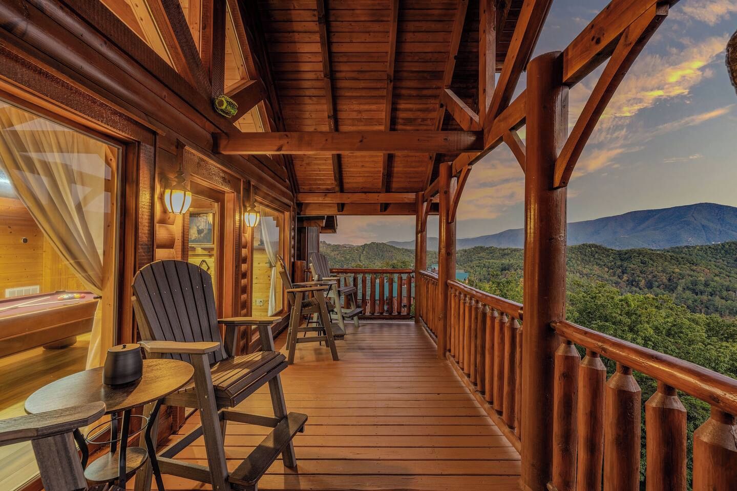 A wooden deck with a pool table, chairs, and a view of a mountainous landscape.