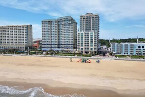 Un hotel frente a la playa con varios edificios altos, una playa arenosa y un parque infantil.