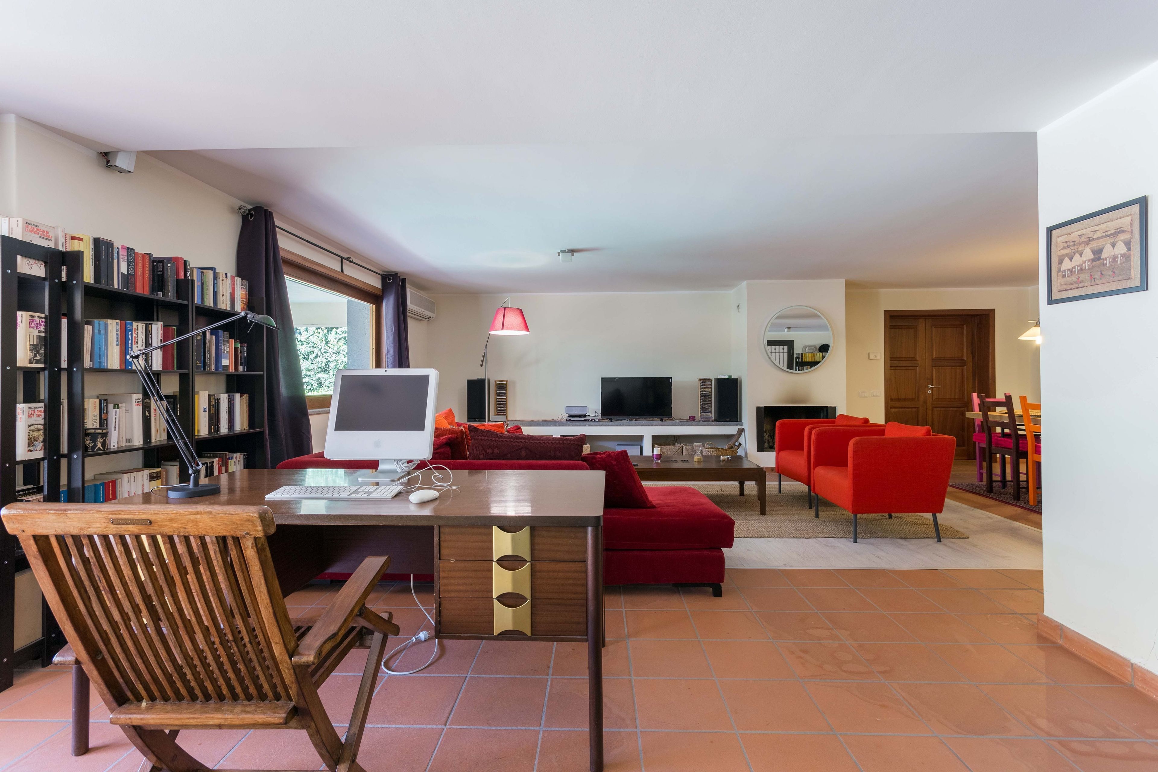 A living room with a desk, a red sofa, a television, and a bookshelf.