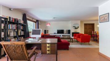 A living room with a desk, a red sofa, a television, and a bookshelf.
