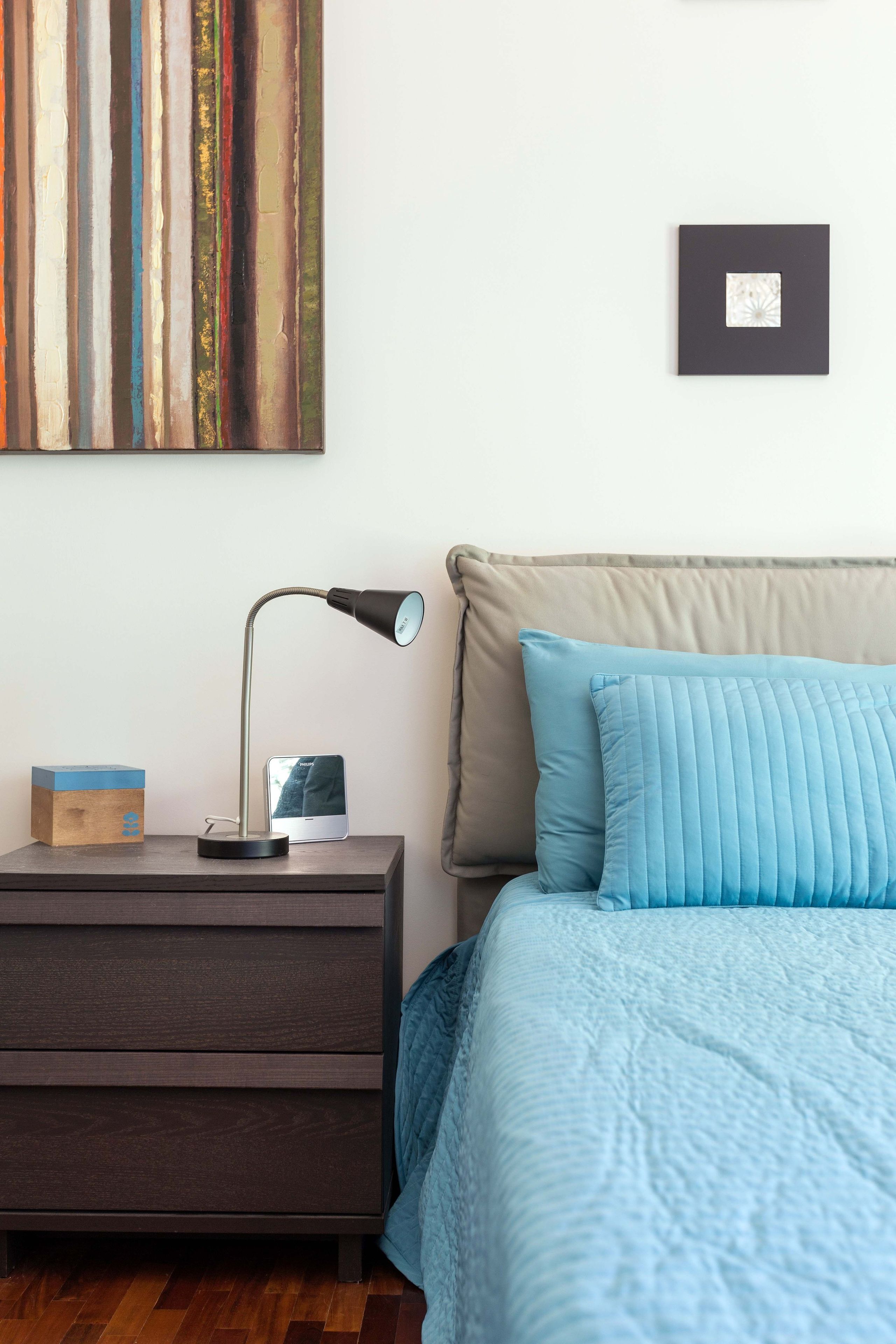 A neatly arranged bedroom with a bed, a nightstand, a lamp, and a wall-mounted picture frame.