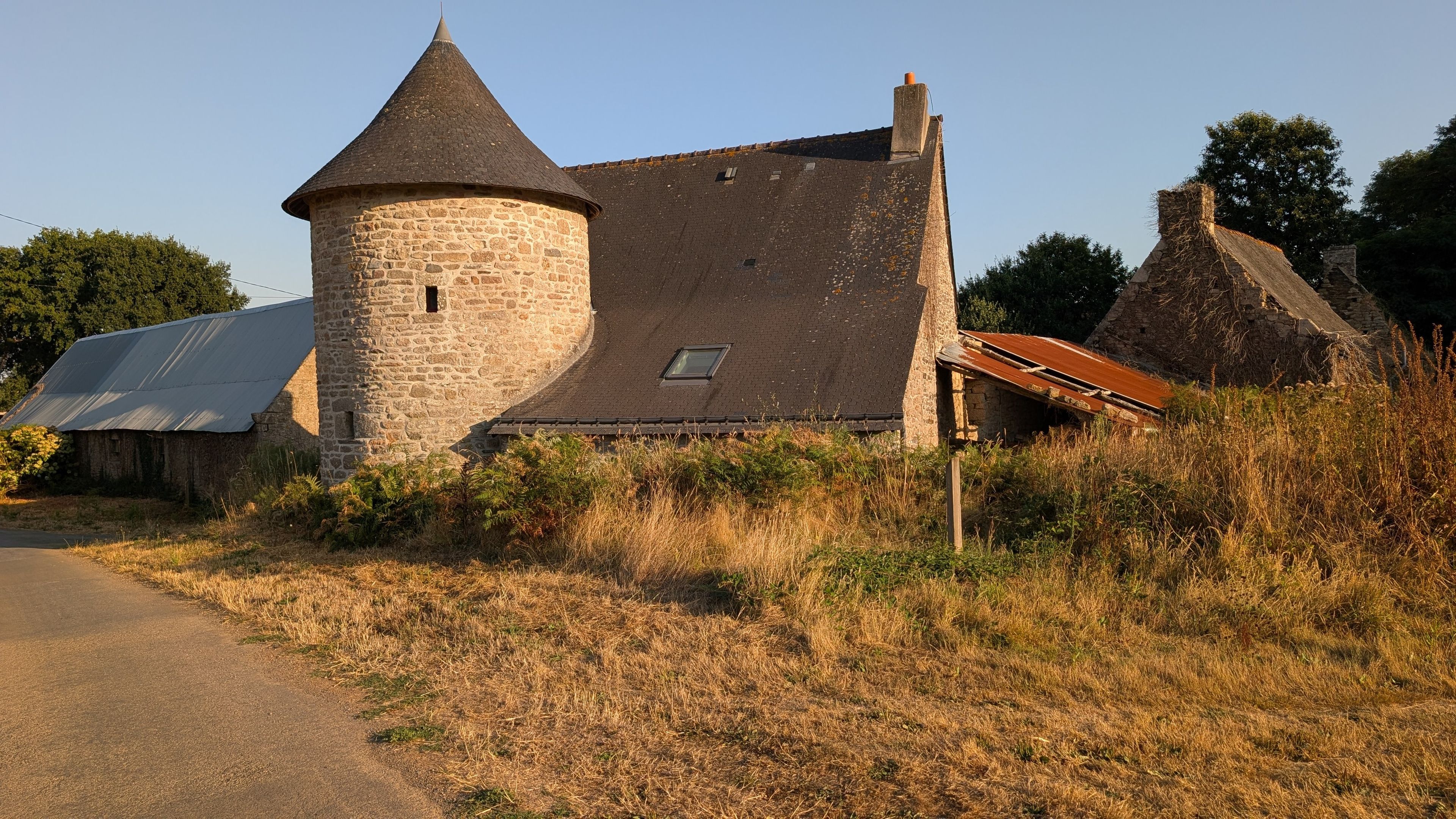 A stone tower with a conical roof, a thatched-roof building, and a metal-roofed structure.