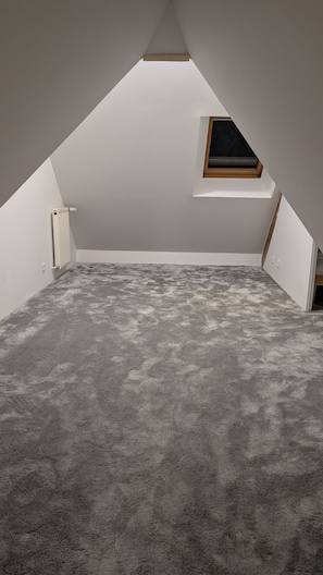 A room with a sloped ceiling, a radiator, a small window, and a grey carpet. - Manoir de Kermarec – A Peaceful Stay between Countryside and Forest in Pontivy (Pontivy)