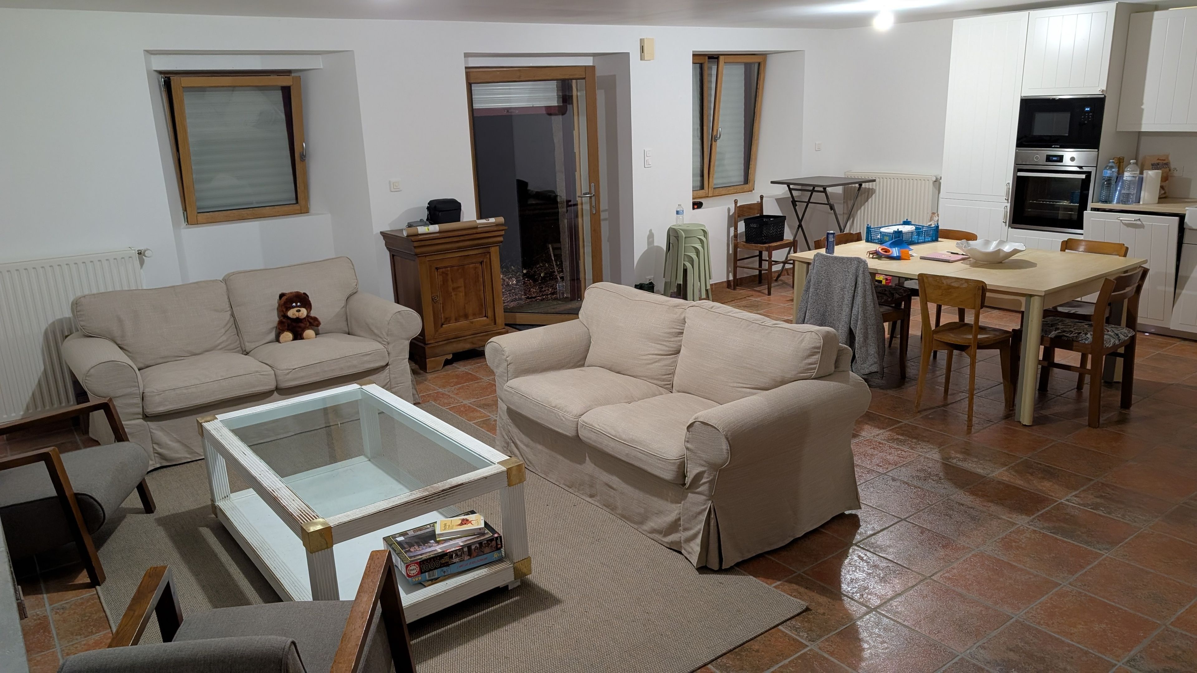 Un salon comprenant un canapé, une table basse avec un plateau en verre et un coin repas avec une table et des chaises.