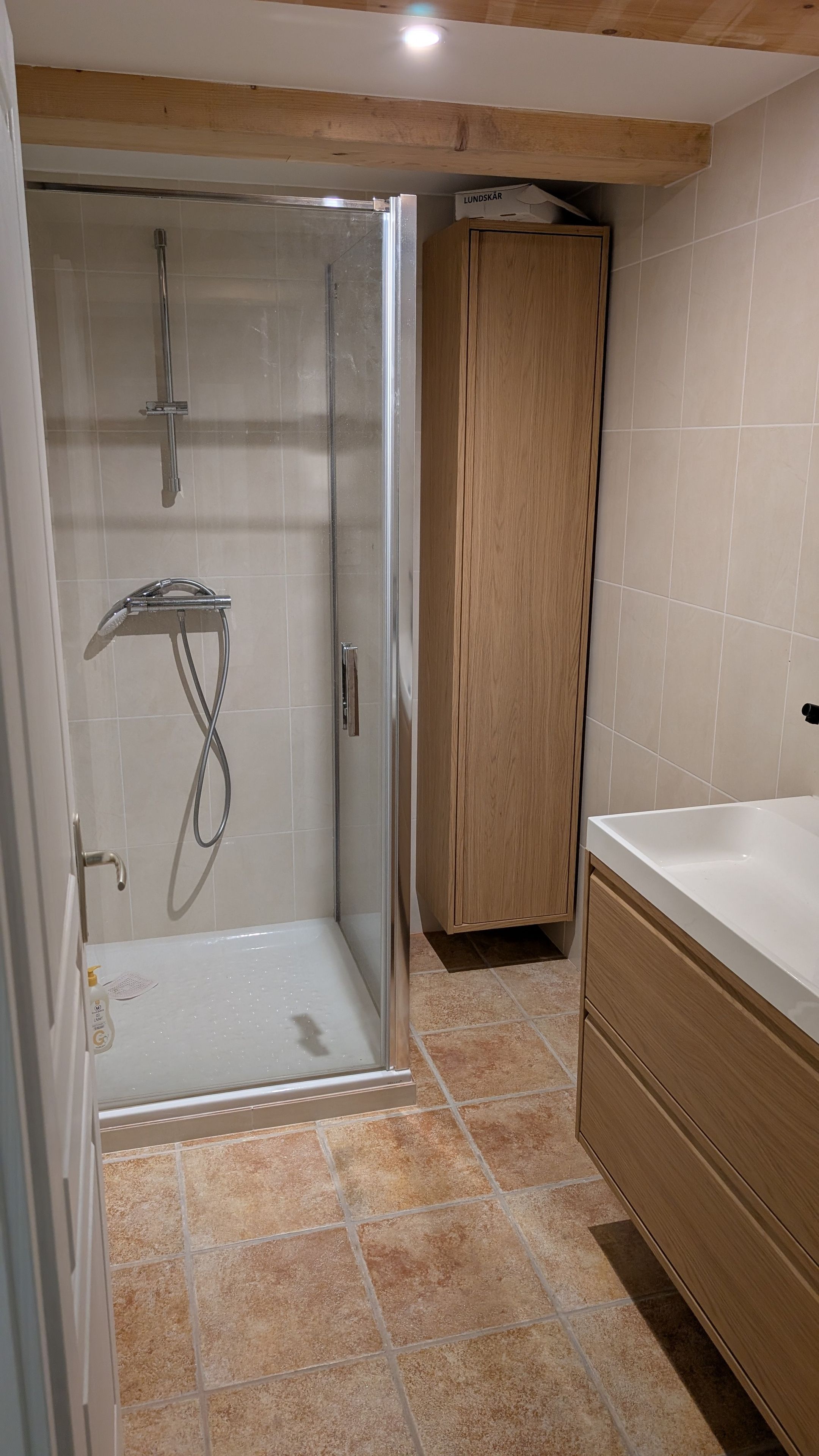 Un baño con ducha de vidrio, un armario de madera y una bañera blanca.