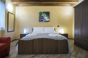 Habitación de hotel con cama de madera, dos mesitas de noche con lámparas, un armario grande y una obra de arte enmarcada en la pared.