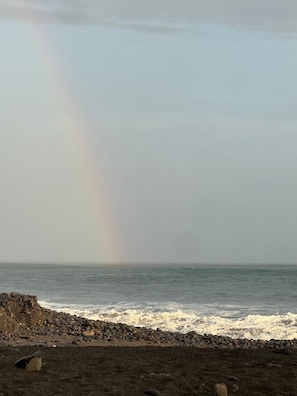 Una platja amb un arc de pluja sobre l'oceà i un litoral rocos.