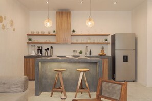 Una cocina moderna con una isla central, taburetes de madera, un refrigerador e iluminación colgante.