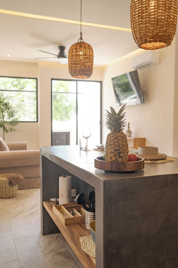 Una cocina moderna con una isla central, una lámpara colgante de mimbre y un televisor montado en la pared.