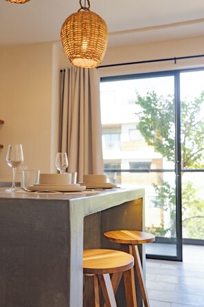 Un comedor moderno con barra de hormigón, taburetes de madera y una lámpara de fibra trenzada.