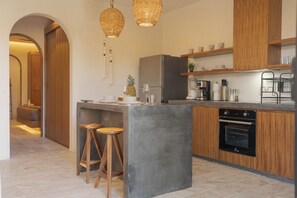 Una cocina moderna con una isla central, taburetes de madera, horno empotrado y cafetera.