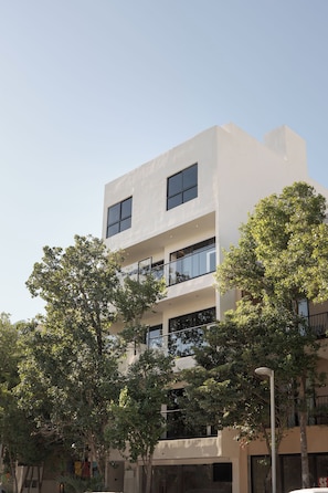 A multi-story building with large windows and balconies, surrounded by trees. - OTONONOMUS TOWER (Tulum)