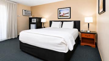 A hotel room with a bed, bedside tables, a desk, a chair, an air conditioning unit, a picture on the wall, and a window with curtains.
