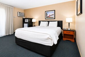 A hotel room with a bed, bedside tables, a desk, a chair, an air conditioning unit, a picture on the wall, and a window with curtains. - Deluxe King with Pool-View Balcony – Downtown Solvang (Solvang)