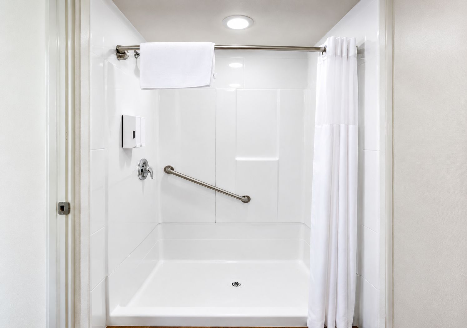 A white bathroom with a shower, a grab bar, and a towel rack.