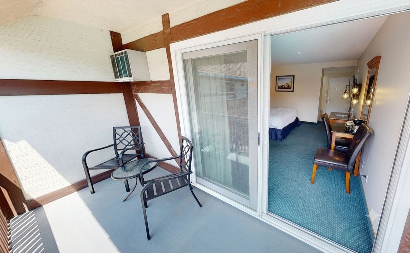 A hotel room with a balcony, a bed, a desk, and a chair.