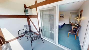 A hotel room with a balcony, a bed, a desk, and a chair.