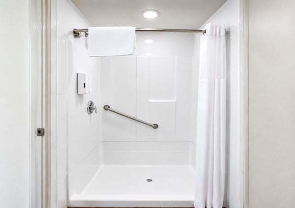 Un baño blanco con ducha, barra de apoyo y toallero.